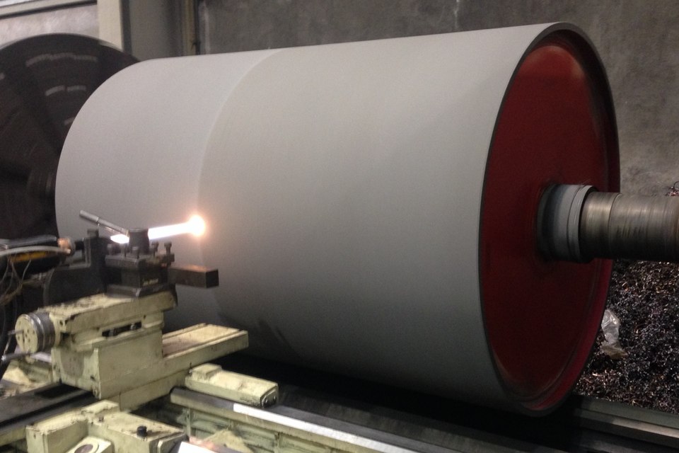 Large industrial roll mounted on a lathe, with a spray jet contacting its surface.